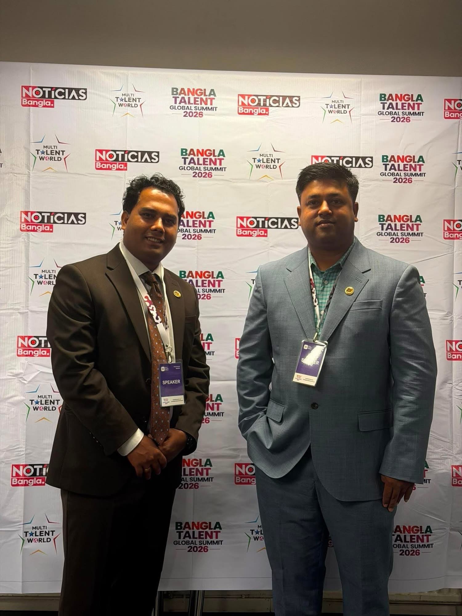 Two guests in suits pose in front of the summit media wall