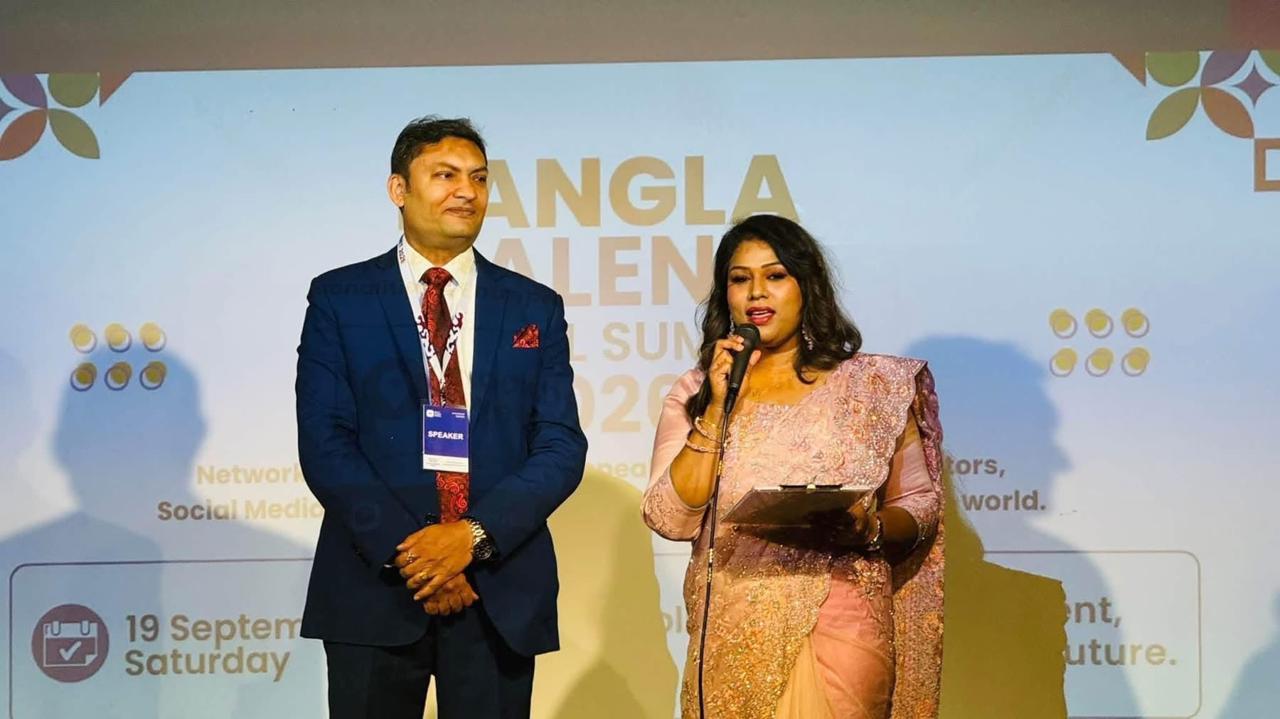 A host in a suit and a host in a sari introduce the programme