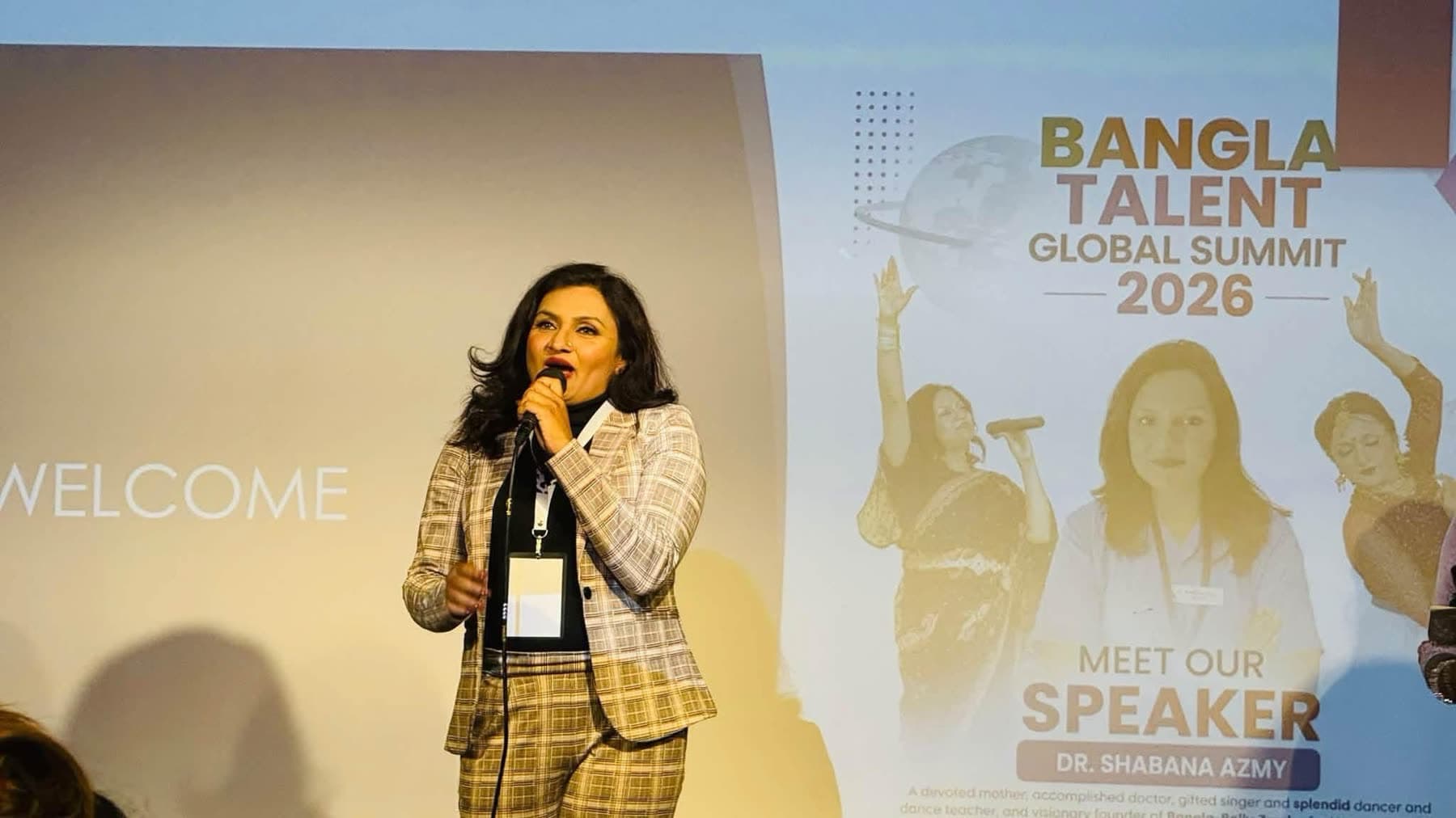 A speaker in a checked jacket talks to the audience in front of her speaker poster