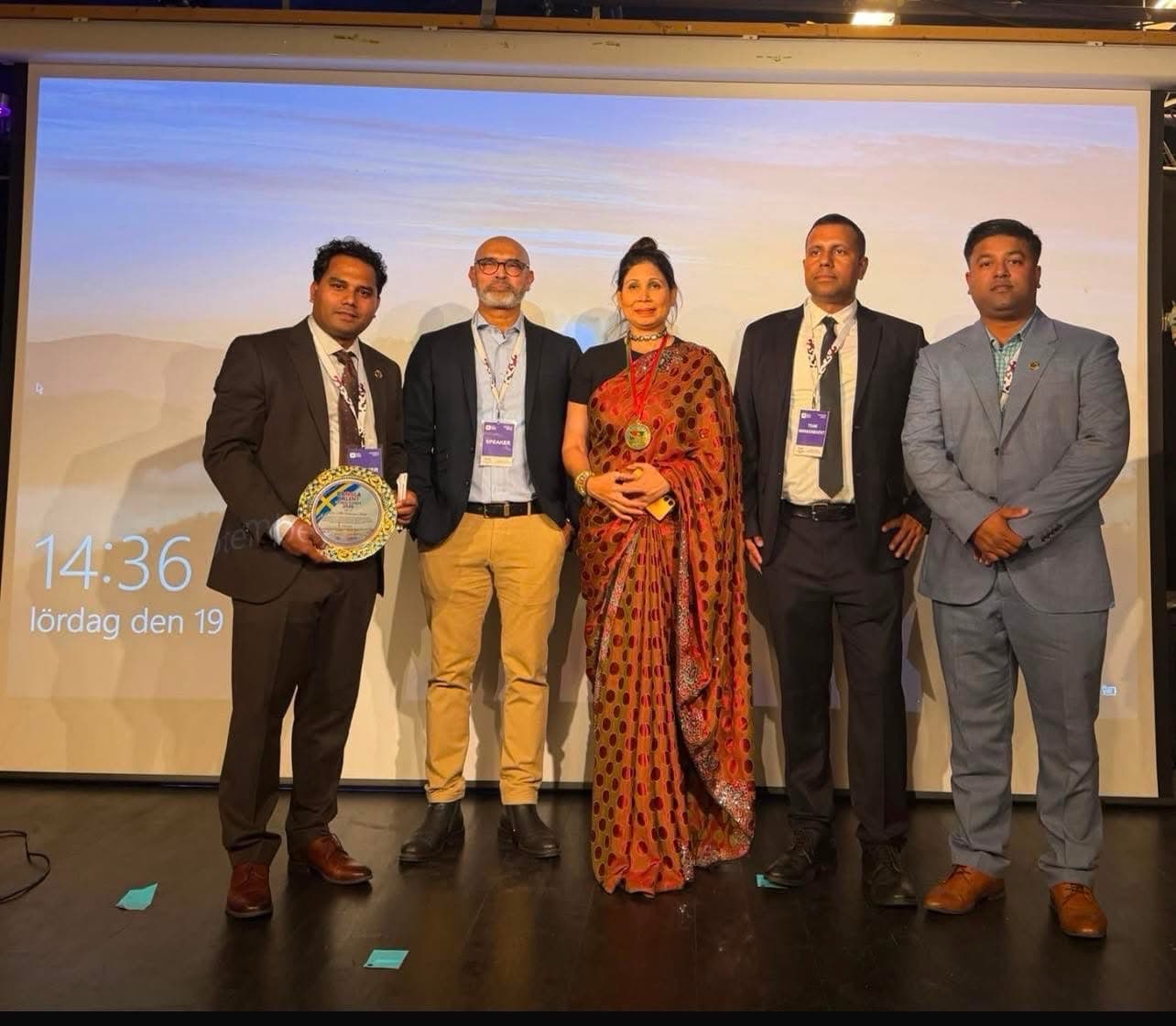 Five people stand on stage while one of them holds an award plaque